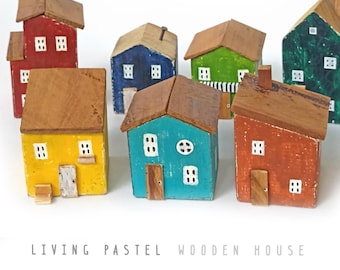 Puede incluir: Una colección de siete pequeñas figuras de casas de madera con techos marrones y paredes pintadas en rojo, azul, verde, amarillo, turquesa y naranja. Cada casa presenta pequeñas ventanas y puertas pintadas de blanco. El texto LIVING PASTEL WOODEN HOUSE es visible.