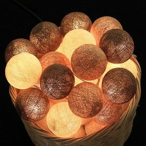 Op de afbeelding: Een mand gevuld met een string ronde, katoenen ballenlichten. De lichten zijn een mix van crème en bruine kleuren.