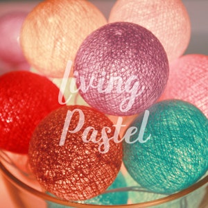 Op de afbeelding: Een verzameling bolvormige lichtsnoeren in diverse kleuren, waaronder rood, roze, paars en talingroen, gerangschikt in een cluster. De tekst "living Pastel" is in wit handschrift over de verlichte, getextureerde bollen heen geplaatst.