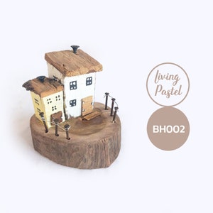 May include: A miniature wooden house with a yellow and white painted exterior, sitting on a wooden base with a fence. The house has a small chimney and a door. The base is made of a tree trunk slice. The text "Living Pastel" and "BHOO2" is visible in the image.
