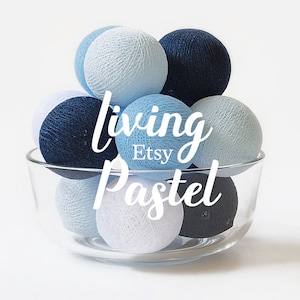 May include: A glass bowl filled with cotton ball lights in shades of blue and white. The lights are arranged in a pyramid shape with the text "living pastel Etsy" printed on the front of the bowl.