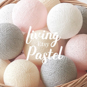 May include: A collection of spherical string lights in a woven basket, featuring a color palette of soft pink, cream, white, and light gray. The text "living Etsy Pastel" is overlaid in white script across the center of the round cotton yarn balls.