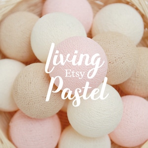 Puede incluir: Una colección de luces suaves y redondas de algodón en tonos pastel rosa, beige y blanco. Las luces están dispuestas en una cesta y el texto "living Pastel Etsy" está superpuesto en la imagen.