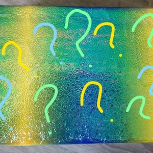 May include: A blue, green, and yellow iridescent box with question marks drawn on it in blue, green, and yellow.