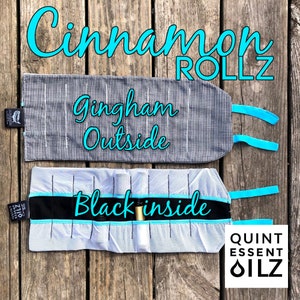 May include: Two essential oil roll cases. The top case is black and white gingham with the text "Gingham Outside". The bottom case is white with black accents and the text "Black inside". Both cases have teal accents and the text "Cinnamon ROLLZ".
