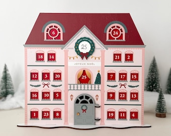 May include: A pink and claret wooden Christmas advent calendar in the shape of a house. It features 24 numbered windows, a wreath on the door, and the text "JOYEUX NOËL". The roof is claret, and the windows are red.