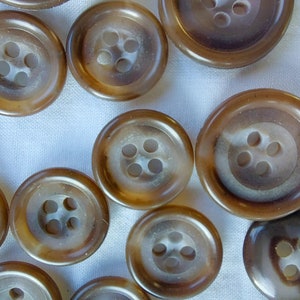 May include: A collection of brown plastic buttons with five holes each. The buttons are arranged in a random pattern on a white surface.
