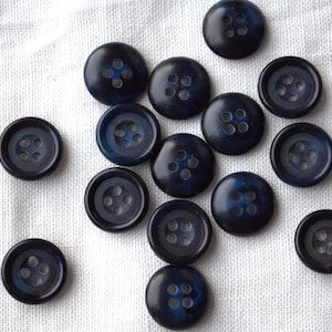 May include: A selection of navy blue buttons, each with four holes, arranged on a white, textured cloth. The buttons display a marbled effect. Suitable for sewing and craft projects. The buttons are approximately 1.5 cm in diameter.