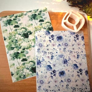 May include: Two sheets of decorative paper with watercolor floral patterns. One sheet features a green and white floral pattern, while the other sheet features a blue and white floral pattern.