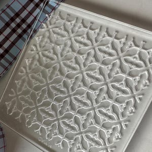 May include: A clear glass square serving tray with a raised embossed pattern of a repeating geometric design.