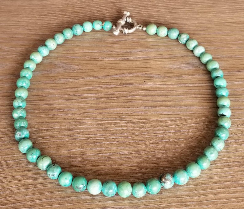 May include: A turquoise beaded necklace with a silver clasp. The beads are round and uniform in size.