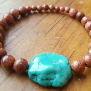May include: A brown beaded bracelet with a large turquoise stone charm.