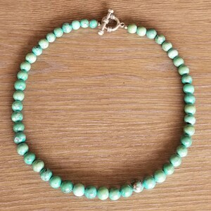 May include: A turquoise beaded necklace with a silver toggle clasp. The necklace is made of round beads and is approximately 18 inches long.
