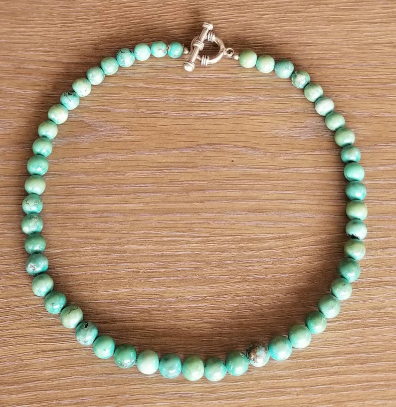 May include: A turquoise beaded necklace with a silver toggle clasp. The necklace is made of round beads and is approximately 18 inches long.