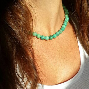 May include: A turquoise beaded necklace with round beads. The necklace is worn by a person with long brown hair.