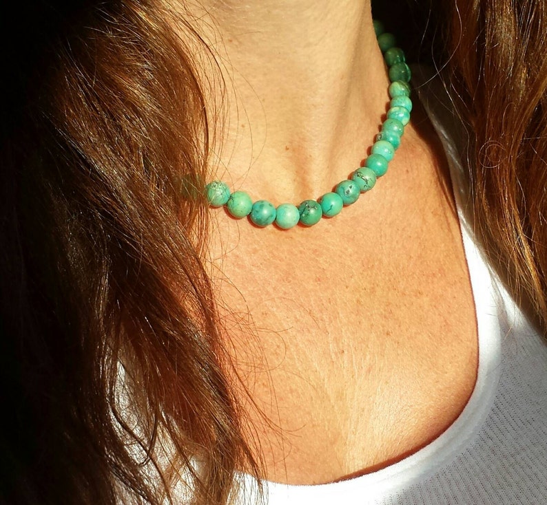 May include: A turquoise beaded necklace with round beads. The necklace is worn by a person with long brown hair.