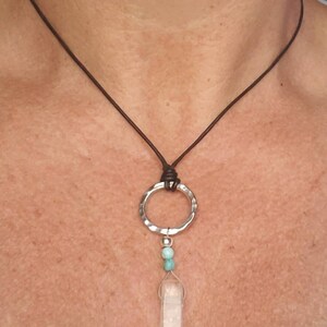 May include: A silver pendant necklace with a clear crystal point, two turquoise beads, and a hammered silver circle. The necklace is on a brown leather cord.