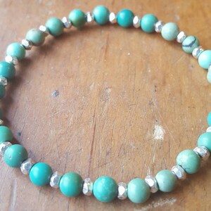 May include: A turquoise and silver beaded bracelet. The bracelet is made with round turquoise beads and silver spacer beads.
