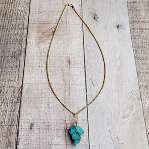 May include: A gold chain necklace with a turquoise stone pendant. The stone is a rough, irregular shape and is wrapped in gold wire.