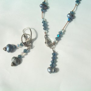 May include: A blue pearl necklace with a silver clasp and matching earrings. The necklace features blue crystal beads and the earrings have silver hooks.