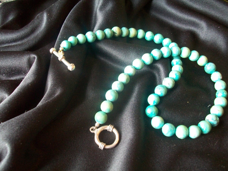 May include: A turquoise blue beaded necklace with a silver clasp and a silver toggle closure.