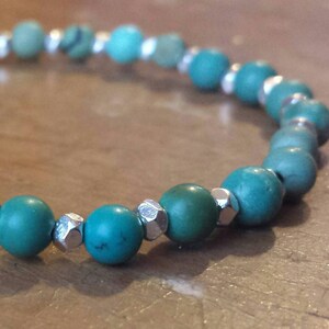 May include: A turquoise and silver beaded bracelet with a simple design. The bracelet is made with round turquoise beads and silver spacer beads.