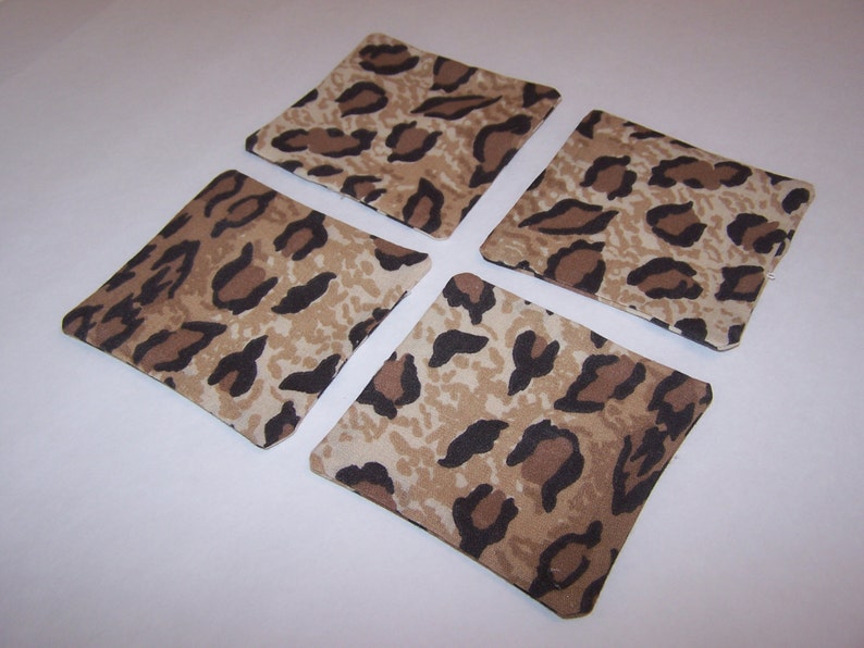May include: Four square fabric coasters with a brown and beige leopard print design.