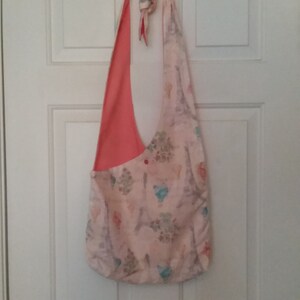 May include: A pink and white fabric tote bag with a coral pink lining. The bag has a long strap and a floral pattern with Eiffel Towers.