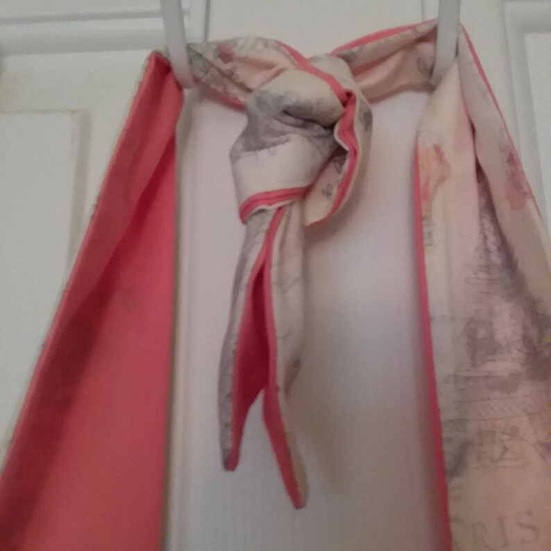 May include: A pink and white scarf with a floral pattern. The scarf is tied in a knot and hanging from a hook.