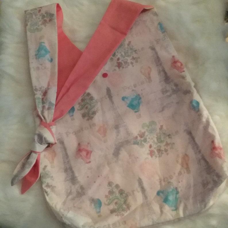 May include: A pink and white fabric tote bag with a pink tie closure. The bag features a print of the Eiffel Tower and other Parisian-themed imagery.
