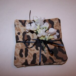 May include: A set of four brown and black leopard print fabric coasters with a white flower tied with a black ribbon.