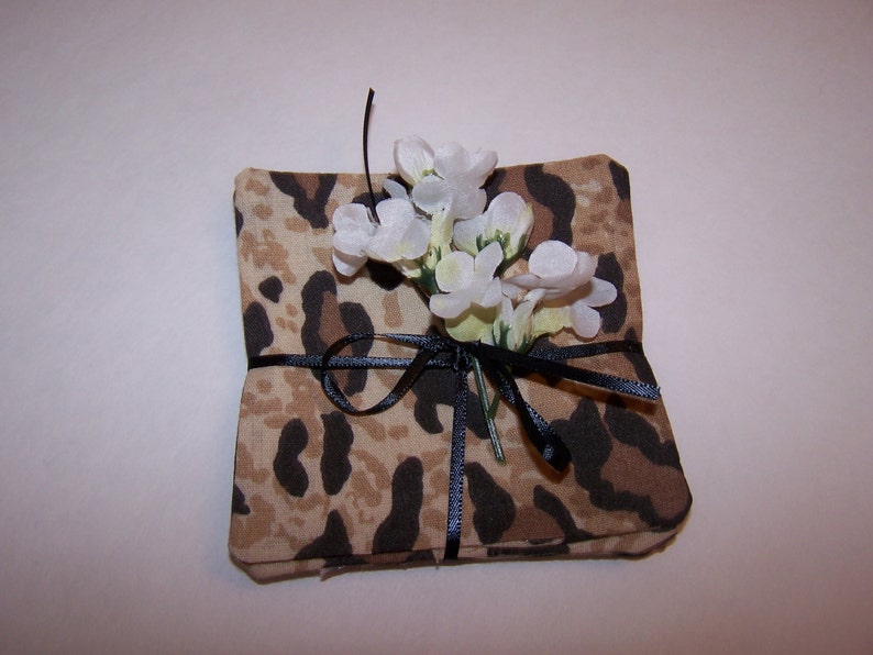 May include: A set of four brown and black leopard print fabric coasters with a white flower tied with a black ribbon.