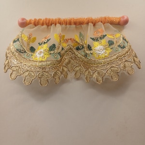 May include: A decorative valance with floral embroidery in yellow, green, and orange, accented with gold trim. The valance is attached to a peach-colored wooden rod with orange fabric.