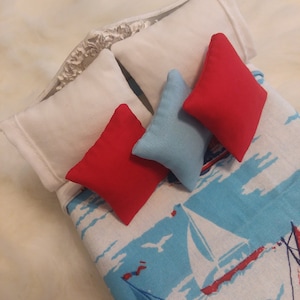 May include: A white bed with a blue and red patterned bedspread. The bed has two white pillows and three decorative pillows. Two of the pillows are red and one is blue.
