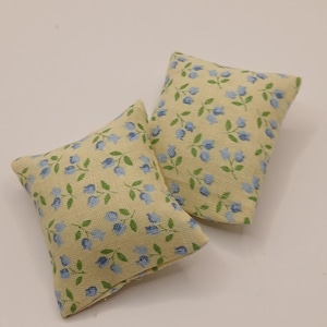 May include: Two small, rectangular cushions with a pale yellow background and a pattern of blue flowers and green leaves. The cushions are made of fabric and appear to be decorative.