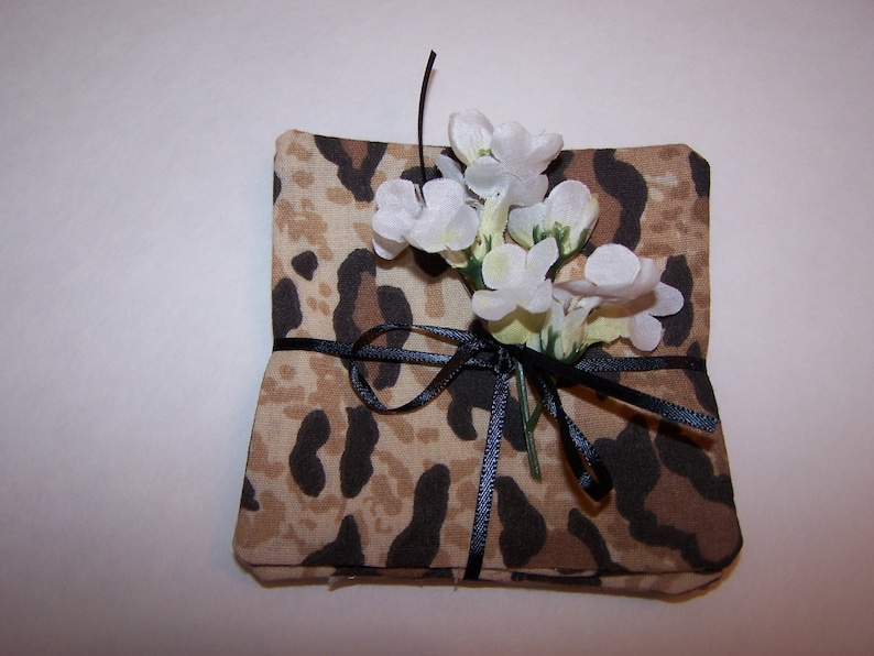 May include: A small gift box wrapped in brown fabric with a leopard print pattern. The box is tied with a black ribbon and decorated with white flowers.