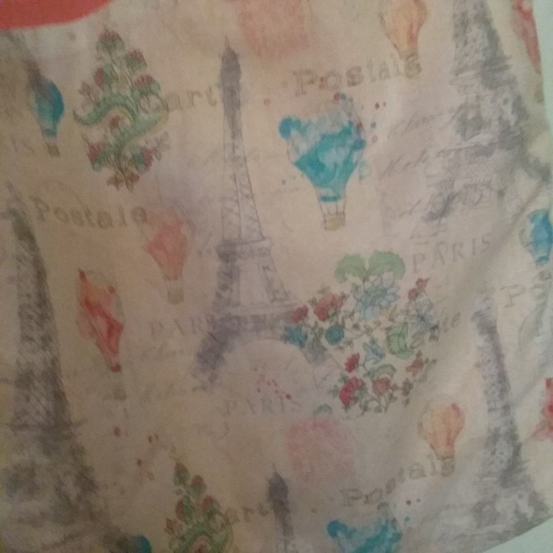 May include: A beige fabric with a repeating pattern of hot air balloons, the Eiffel Tower, and floral bouquets. The fabric has the words "Postale" and "Paris" printed on it.