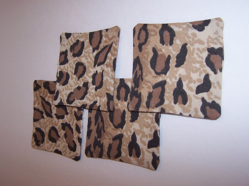 May include: Four brown and black leopard print fabric coasters. The coasters are square shaped and have a light brown background with dark brown spots.