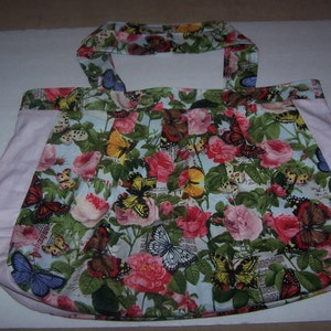 May include: A large tote bag with a pink fabric lining and a blue and white floral print featuring butterflies and roses. The bag has a single strap.