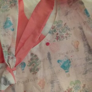 May include: A pink and white fabric with a floral pattern and a print of the Eiffel Tower. The fabric has a pink button on it and the words "Postal" and "Paris" are printed on the fabric.