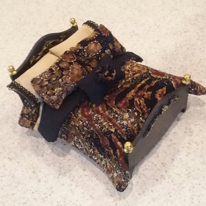May include: A miniature bed with a black and gold patterned comforter and two pillows. The bed has a wooden frame with gold accents.
