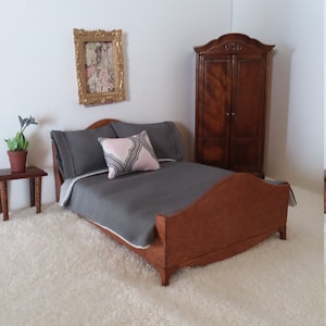 May include: A dollhouse bedroom set with a wooden bed, a gray blanket, a pillow with a pink and gray pattern, a wooden nightstand, a plant, and a wooden armoire with two doors.
