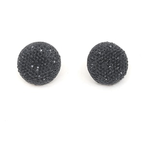 May include: A pair of black, round stud earrings. Each earring is covered in small, sparkling black crystals. The earrings are set against a white background.