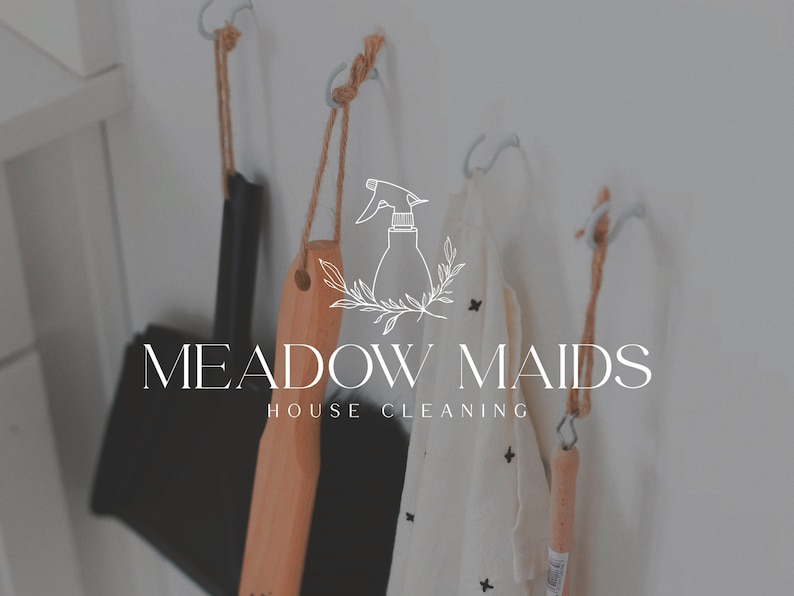 May include: A white wall with three hooks holding cleaning supplies. The hooks are made of metal and have a rope attached to them. The cleaning supplies include a wooden brush, a white cloth, and a spray bottle. The text "MEADOW MAIDS HOUSE CLEANING" is written in white letters on the wall.