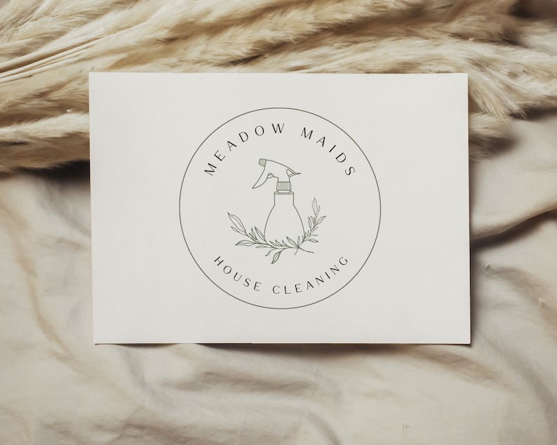 Puede incluir: Un logotipo en blanco y negro para un servicio de limpieza de casas llamado "Meadow Maids House Cleaning". El logotipo presenta una ilustraci&oacute;n estilizada de una botella de spray con hojas.