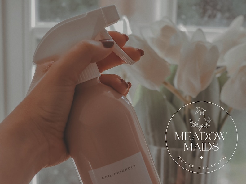 May include: A hand holding a light brown spray bottle with a white trigger and the text "ECO FRIENDLY" on the label. The bottle is in front of a white orchid plant and a round logo that says "MEADOW MAIDS HOUSE CLEANING".