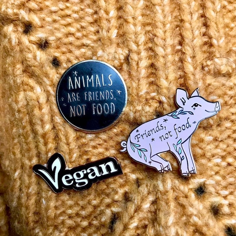 A close up of the three enamel pins attached to someone’s yellowish knitted sweater.