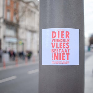 Puede incluir: Un cartel blanco con texto rojo en un poste gris. El cartel dice "DIER VRINDELIJK VLEES BESTAAT NIET.  VEGAN.  EET ALLEEN PLANTENVOEDING.  YOUR MIND, DIET & PLANET."