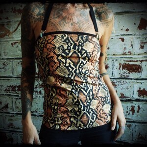 Peut inclure: Un haut sans manches à imprimé serpent dans des tons de brun, noir et blanc. Le haut a une bande noire en haut et de fines bretelles noires.