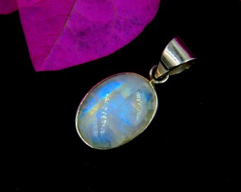 May include: Oval-shaped moonstone pendant with a silver setting. The moonstone displays a blue and yellow iridescent sheen. The pendant is suspended from a silver bail. The background is black with a purple leaf.